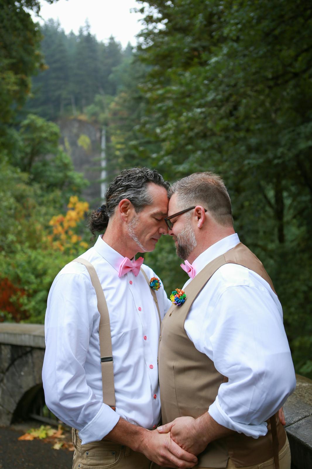 Two grooms sharing a tender moment by a waterfall